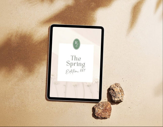 Digital tablet displaying 'The Spring Edition' on a sandy surface with rocks and plant shadows.